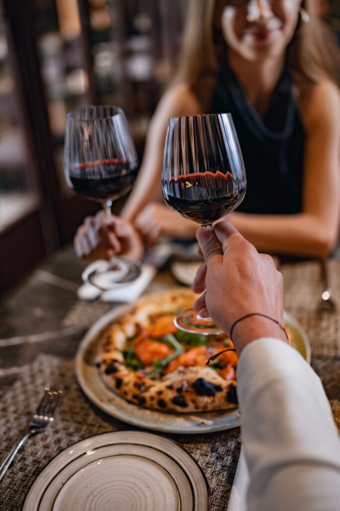 Guests raising glasses of wine over pizza