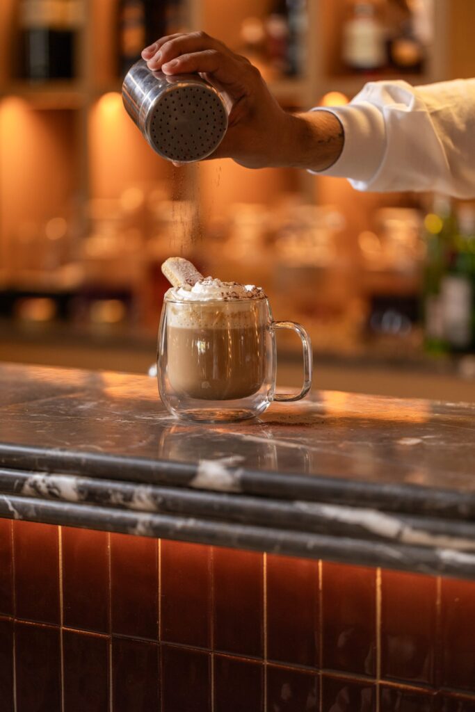 Barista sıcak içeceğin üzerine kakao serpiyor